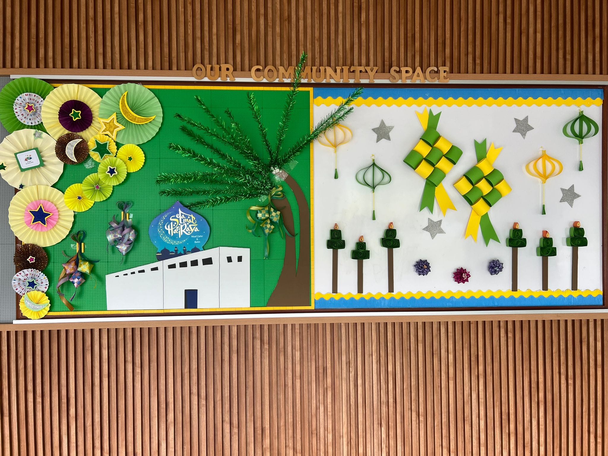 Colorful Hari Raya bulletin board display with paper fans, ketupat, lanterns, and a mosque under "Our Community Space."